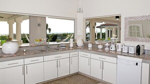 A modern kitchen with white cabinets, granite countertops, and a view of the ocean. - Giselle   Stunning ocean views (Saint Martin)