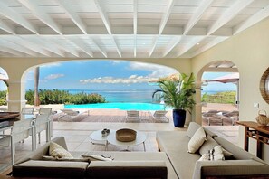 Eine sonnendurchflutete Terrasse mit Meerblick, Gartenmöbeln und einem Pool.