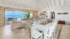 A spacious living area with a large dining table, white chairs, and a view of the ocean through a glass door. - Happy Bay   Classic French Creole Villa   Stunning Views (Saint Martin)