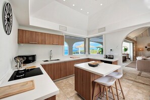 A modern kitchen with wooden cabinets, a white countertop, and a large window offering a view of the outdoors. - Happy Bay   Classic French Creole Villa   Stunning Views (Saint Martin)