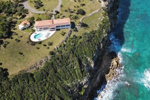 Eine Luftaufnahme eines Anwesens an der Küste mit einem großen Haus, einem Schwimmbad und üppiger Vegetation.