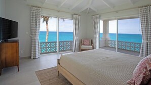 A bedroom with a large bed, a TV, and a view of the ocean. - Falaise des Oiseaux   Clifftop villa with Stunning Views (Saint Martin)