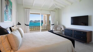 A bedroom with a large bed, a TV, a chair, and a view of the sea. - Falaise des Oiseaux   Clifftop villa with Stunning Views (Saint Martin)