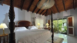 Een slaapkamer met een groot bed, houten balken in het plafond en uitzicht op groen.