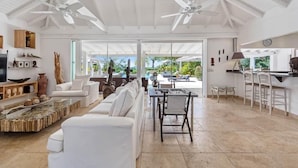 A spacious living area with a white sofa, a dining table with chairs, ceiling fans, and large windows offering a view of the outdoors. - La Pinta   Elegant Creole Style Villa (Saint Martin)