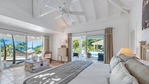 A spacious bedroom with a large bed, a ceiling fan, and a view of a pool and tropical landscape through large sliding doors. - La Pinta   Elegant Creole Style Villa (Saint Martin)