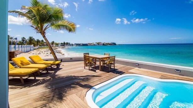 Zona de piscina con sillones amarillos y una mesa, con vista a una playa y al océano.
