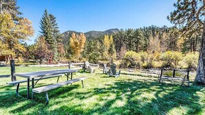 Un área de picnic con bancos y mesas, rodeada de árboles y una montaña al fondo.
