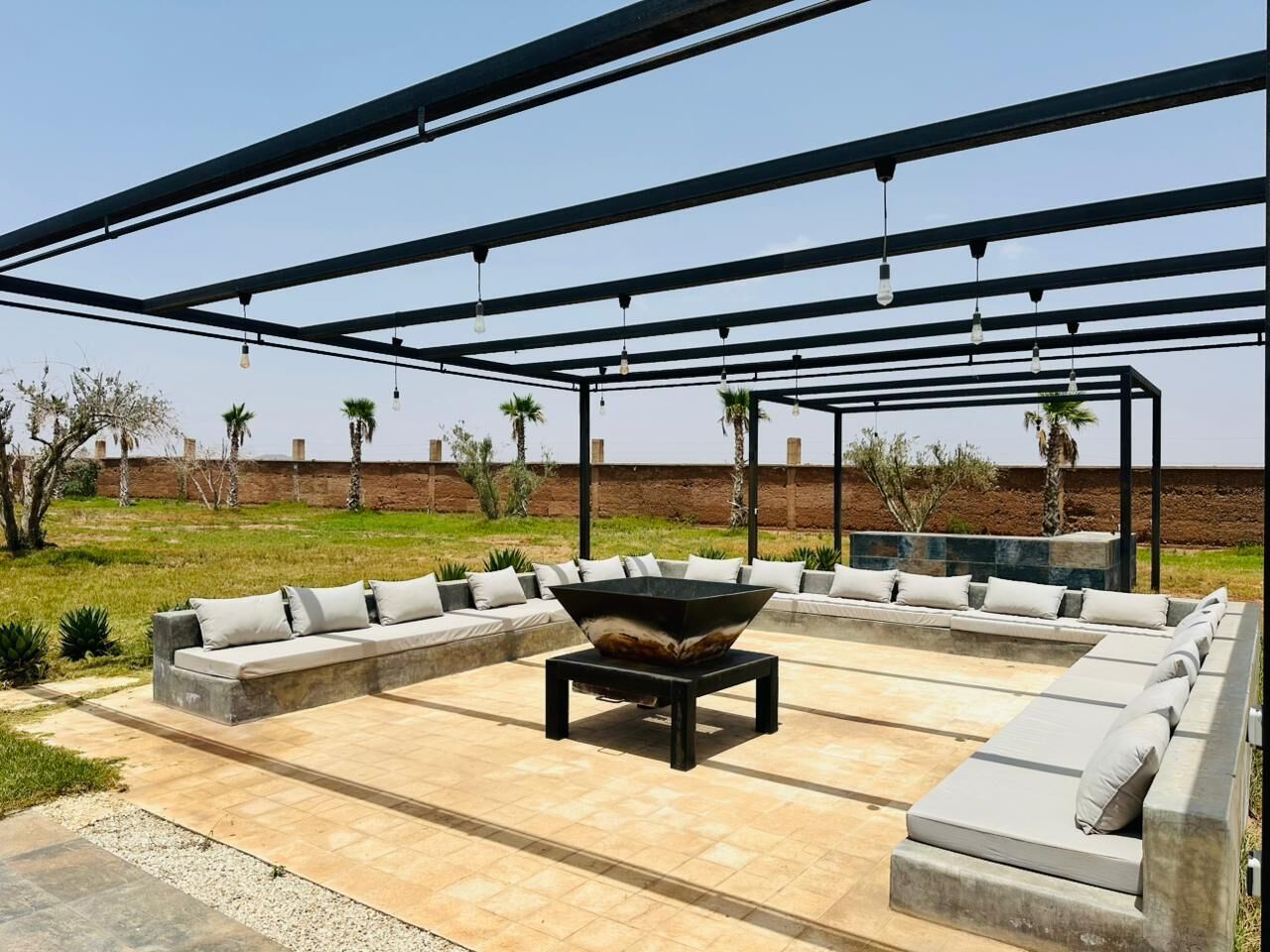 Un patio exterior con un amplio espacio para sentarse, un hogar central y una pérgola en lo alto.
