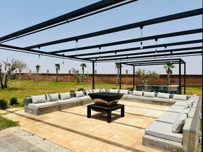 An outdoor patio with a large seating area, a central fire pit, and a pergola overhead. - Luxury villa with heated pool - Private Foot & Padel - Marrakech (Ouled boudden)