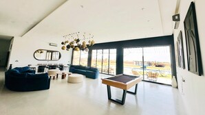 Un vaste espace de vie comprenant une table de billard, des canapés et une grande fenêtre donnant sur l’extérieur.