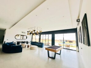 Een ruime woonkamer met een pooltafel, banken en een groot raam met uitzicht op de omgeving.