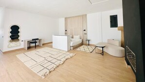 Un salon moderne et bien éclairé, avec un canapé, une petite table, un lit et un téléviseur fixé au mur.