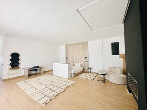 Een moderne, goed verlichte woonkamer met een bank, een kleintje tafeltje, een bed en een tv die aan de muur is bevestigd.