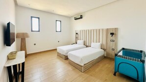 Une chambre moderne avec deux lits simples, un plancher en bois, une petite table avec une lampe et un meuble de rangement bleu.