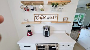 Una cocina con barra de café, que incluye una cafetera, una licuadora y tazas en estantes.
