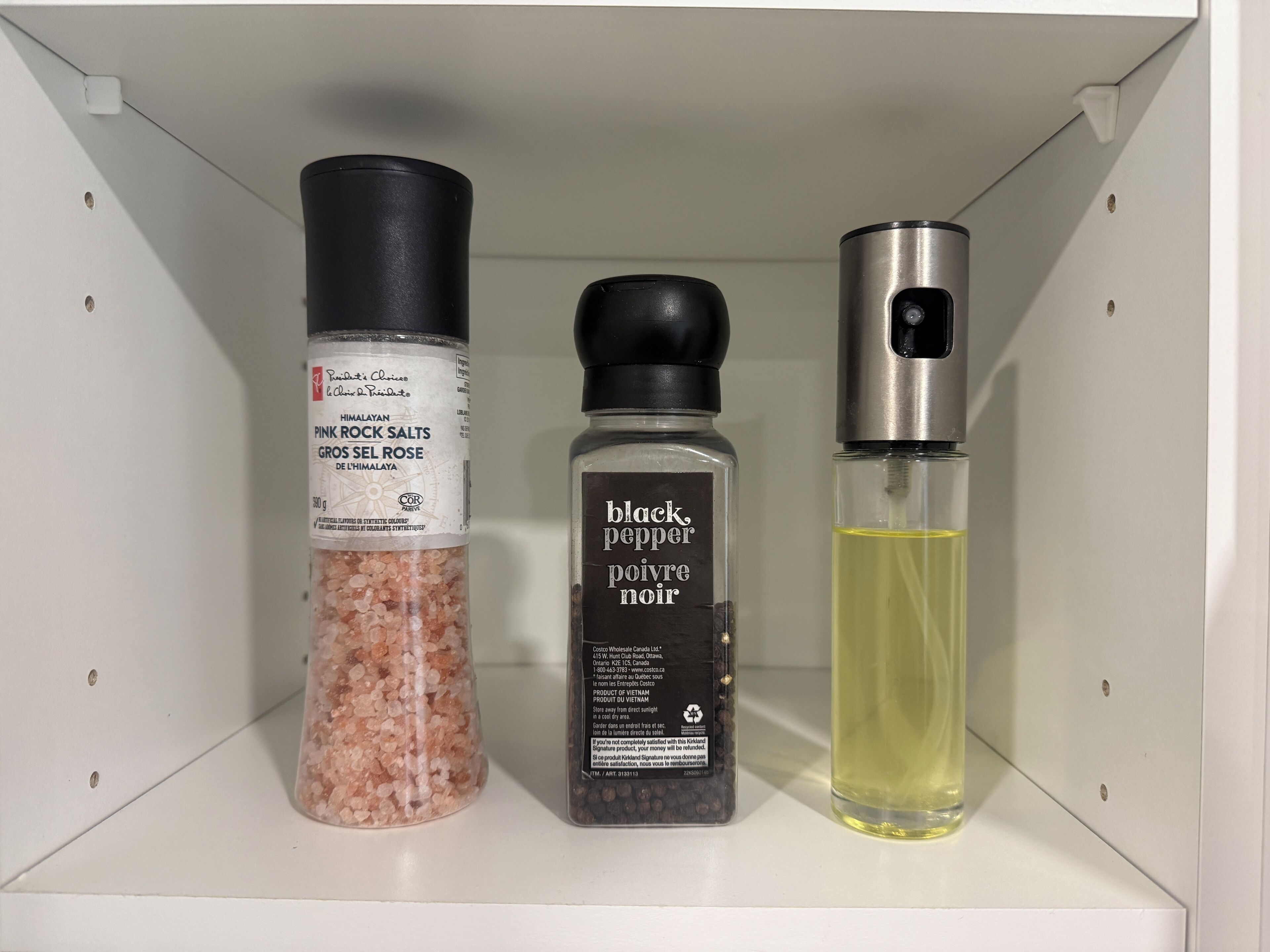 A shelf with three bottles: pink Himalayan salts, black pepper, and a yellow liquid.