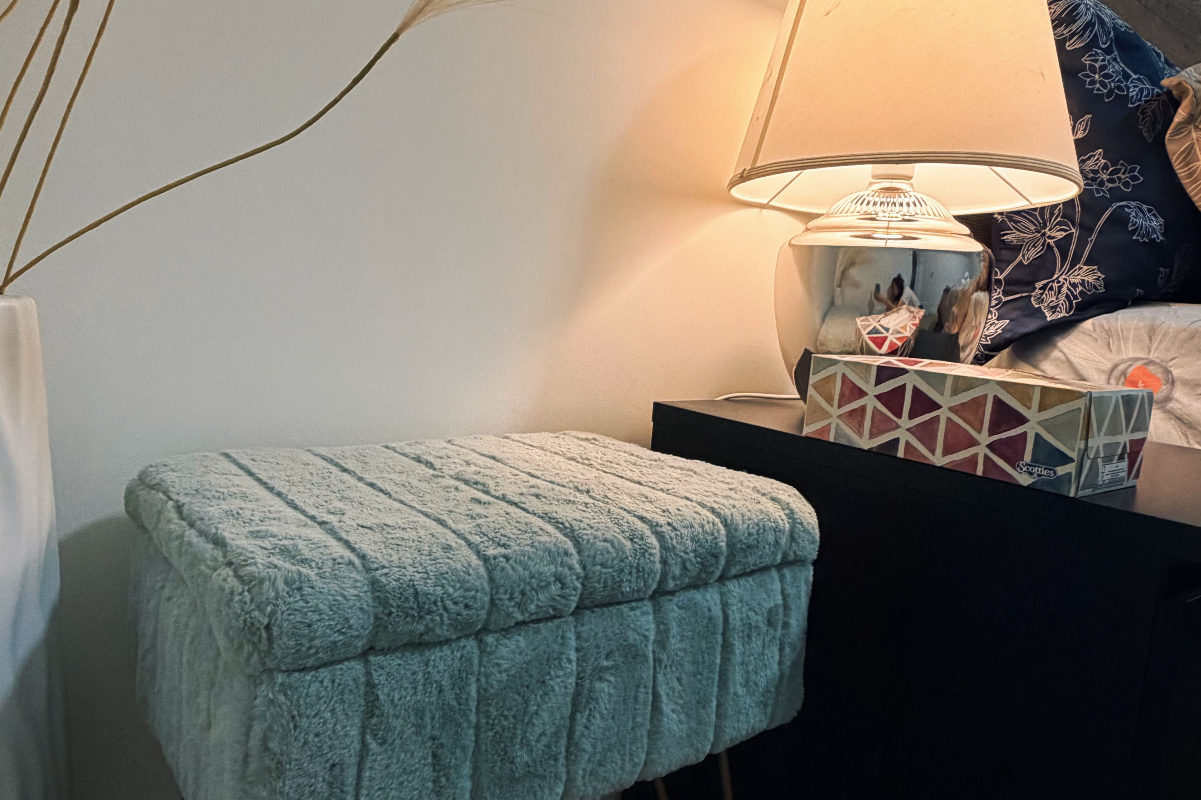 A bedside table with a lamp, a pillow, and a box of tissues.