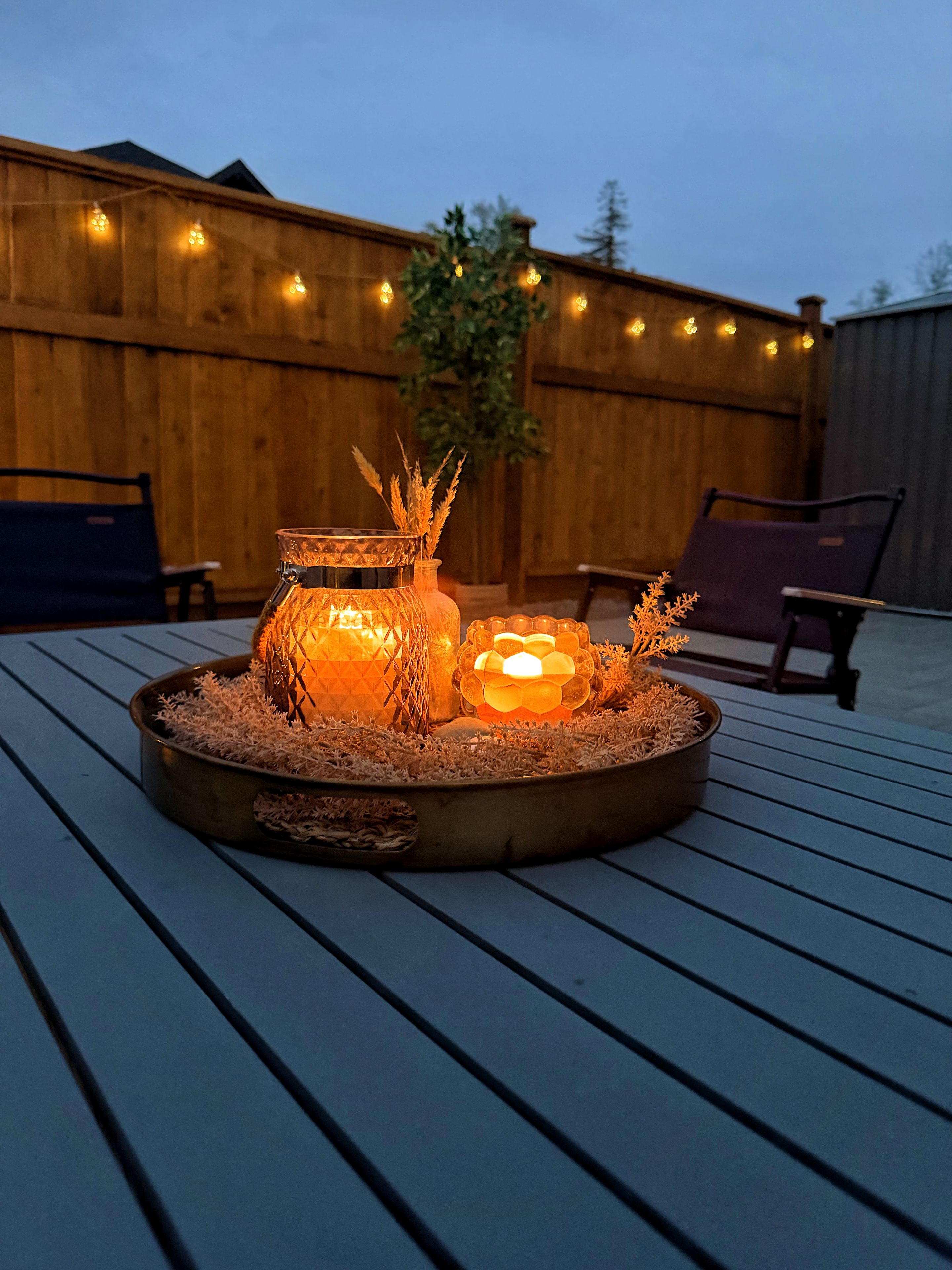 A circular outdoor seating area with a fire feature in the center, surrounded by chairs and a wooden fence in the background.