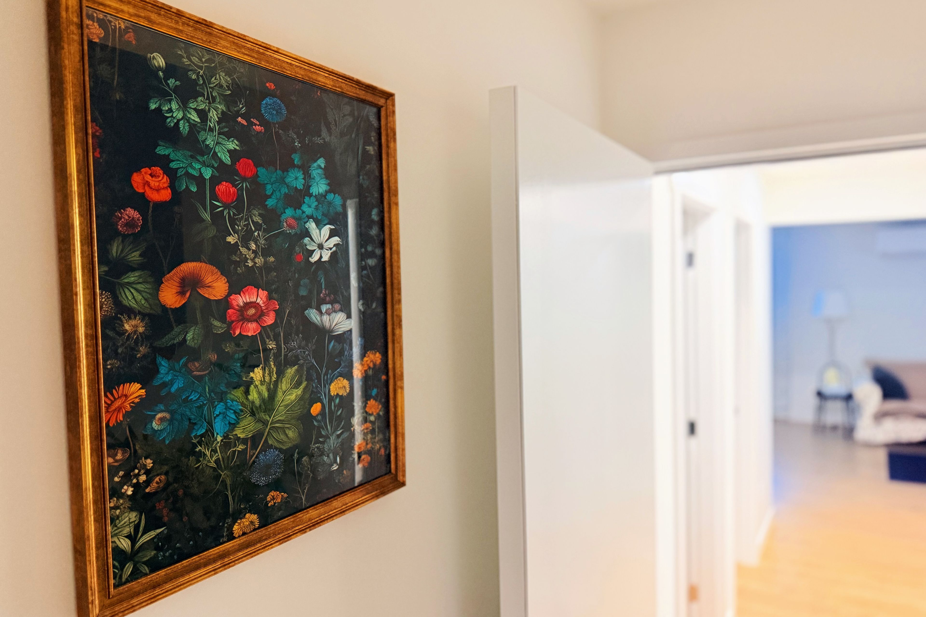 Un couloir orné d’une œuvre d’art florale encadrée au mur, et une porte donnant sur une autre pièce.