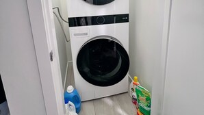 Pieni ja käytännöllinen pyykinhuone, jossa on etuaukosta täytettävä pesukone ja kuivausrumpu, sininen pyykinpesuaineen pullo ja valkoinen pyykinpesuaineen kannu.