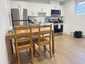 A modern kitchen with white cabinets, stainless steel appliances, and a wooden dining table with chairs.
