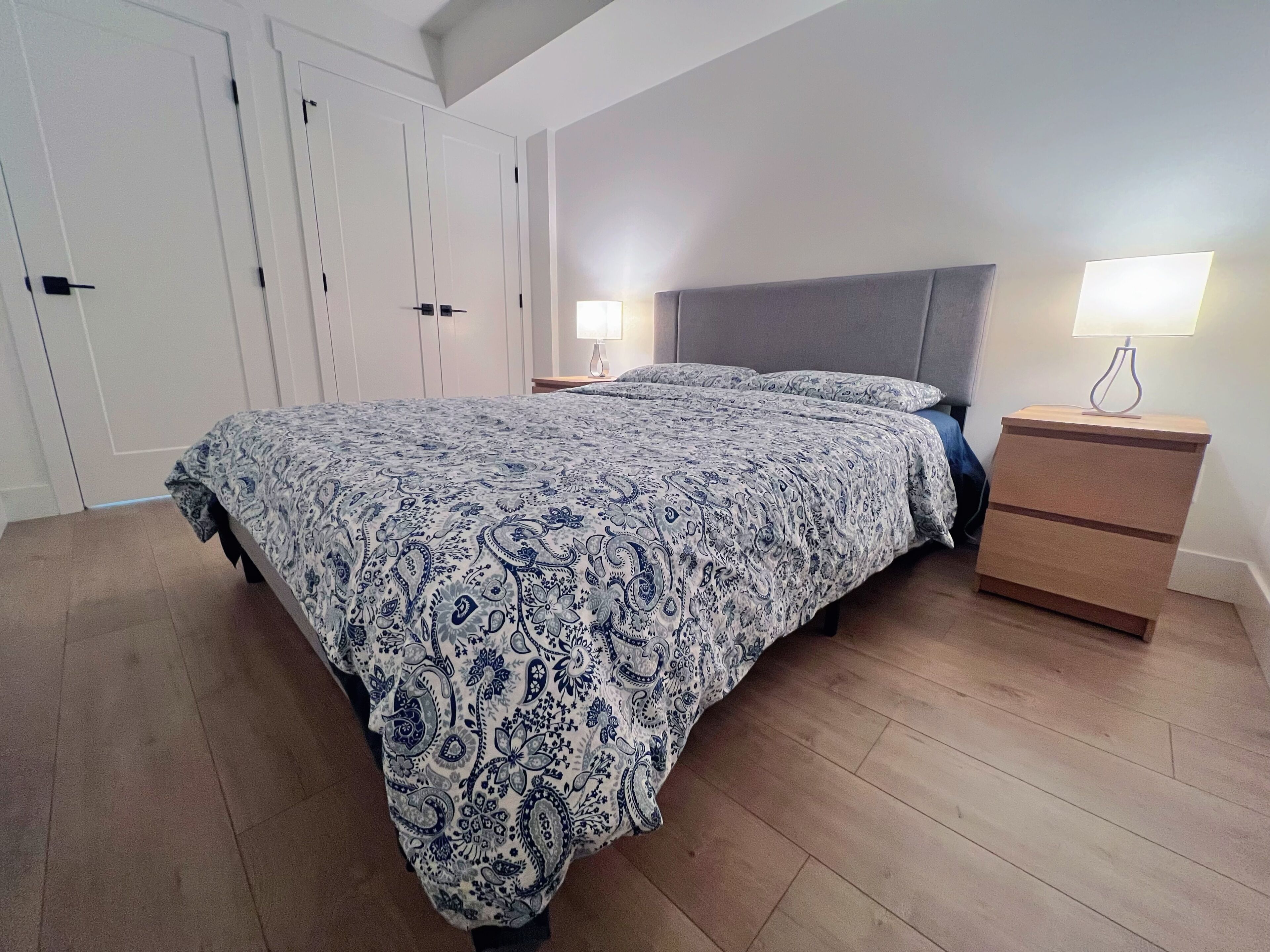 A bedroom with a bed, bedside lamps, a nightstand, and a wardrobe.