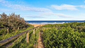 A coastal path leading to a beach with a wooden fence and lush greenery.