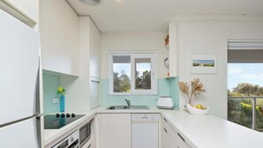 A modern kitchen with white cabinetry, a built-in oven, a dishwasher, and a window above the sink.