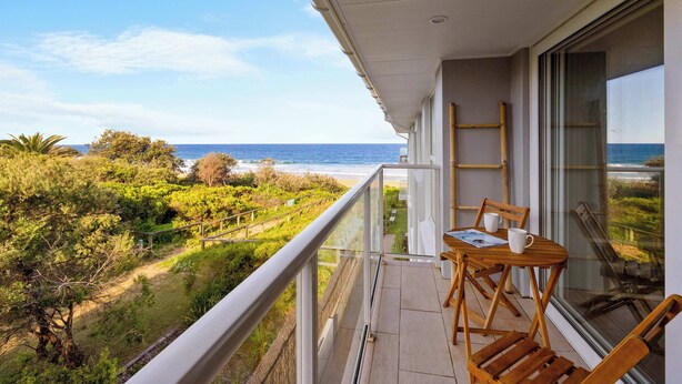 A balcony with a view of the ocean, wooden furniture, and a table with a menu.