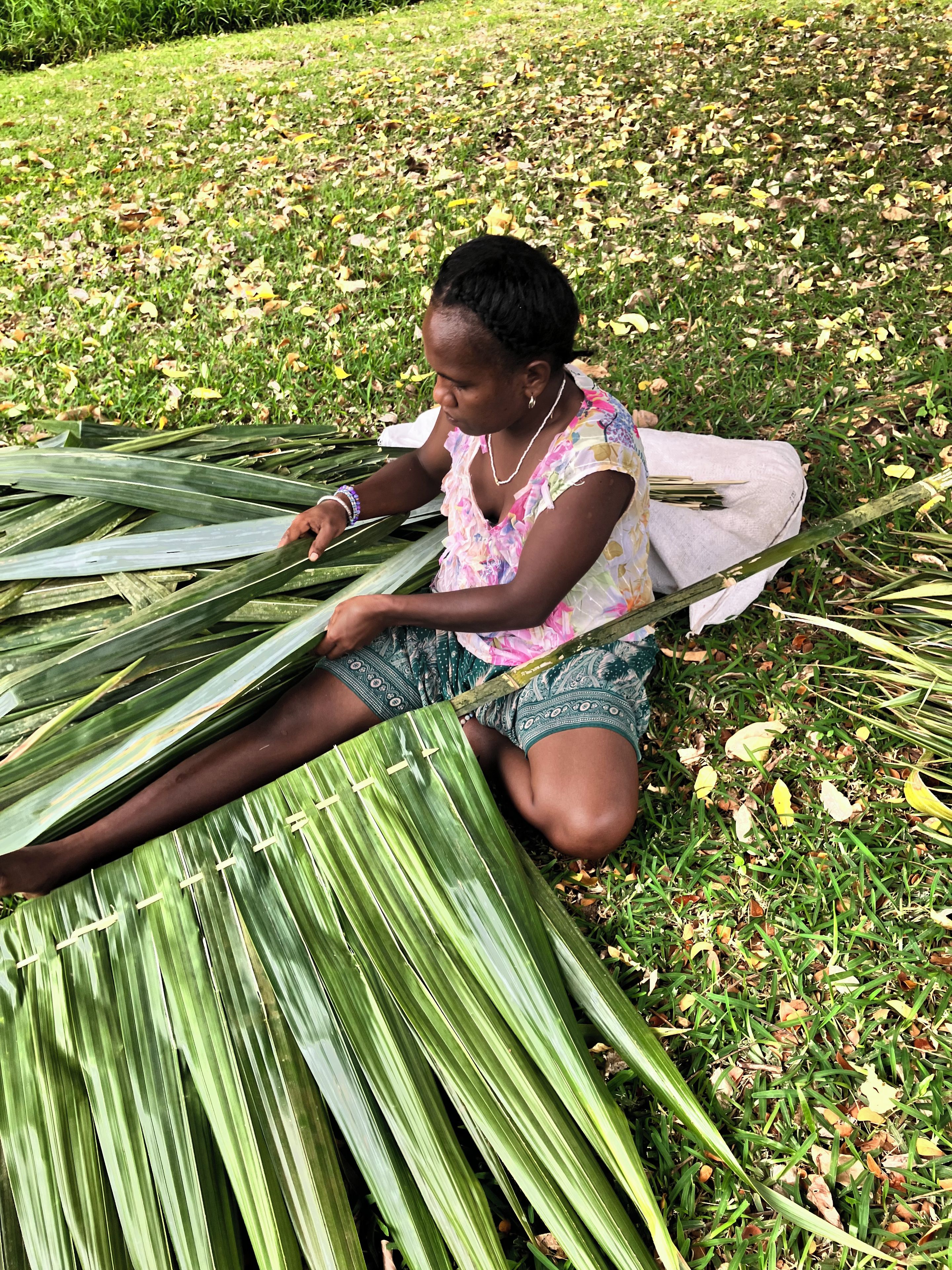 Uma pessoa sentada na grama, rodeada por grandes folhas verdes.