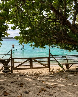 A beach with a wooden fence and a tree providing shade.
