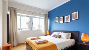 A modern hotel room with a large bed, a nightstand with a lamp, a window with curtains, and framed pictures on the wall. - NEW - Comfortable and central apartment in Lisbon • Between Praça de Espanha and Sete Rios (Lisboa)