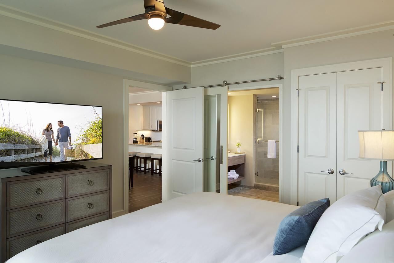 A hotel room with a bed, a television, a ceiling fan, a bathroom with a shower, and a walk-in closet.