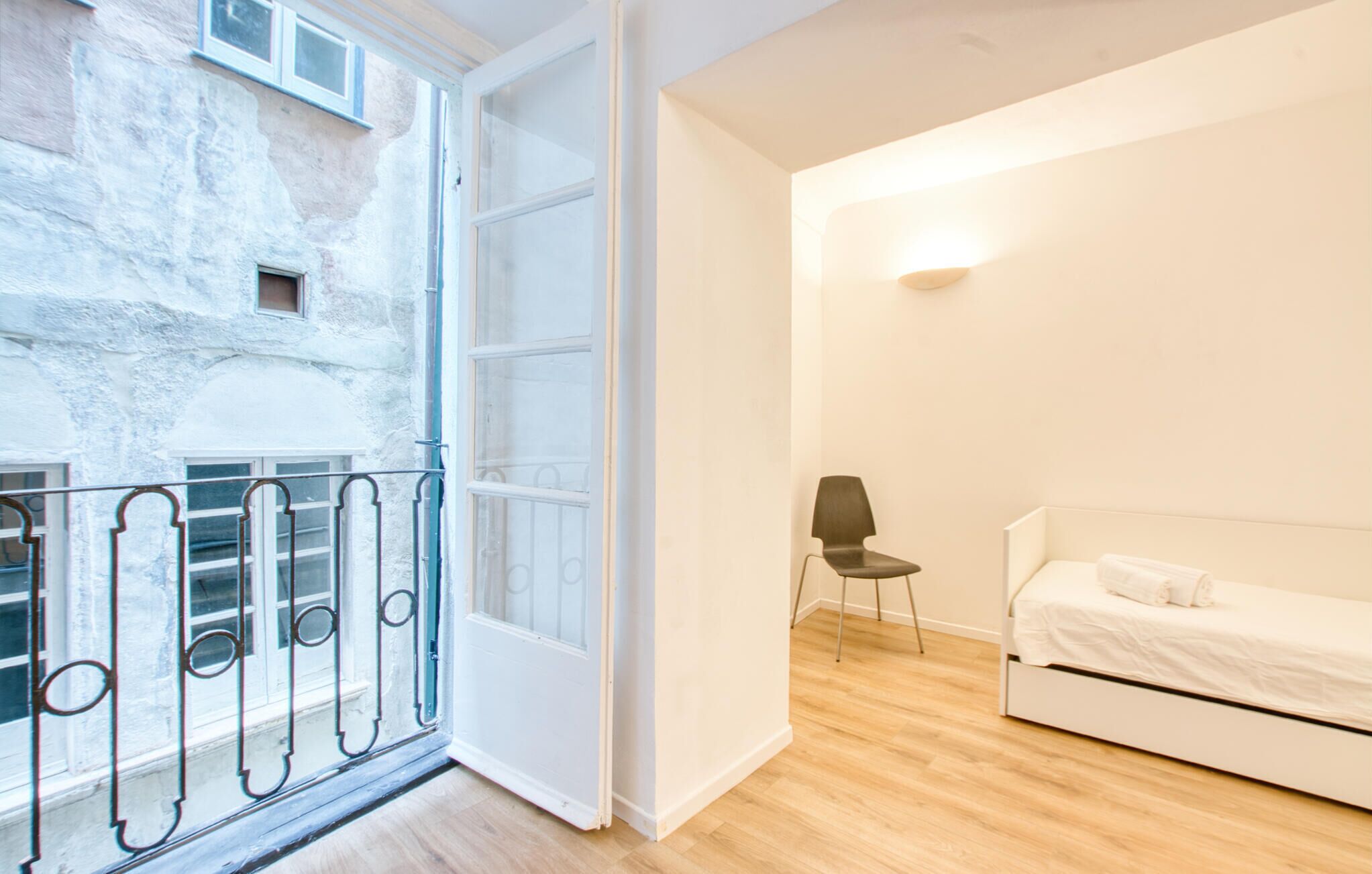A room with a bed, a chair, and a balcony with a metal railing.