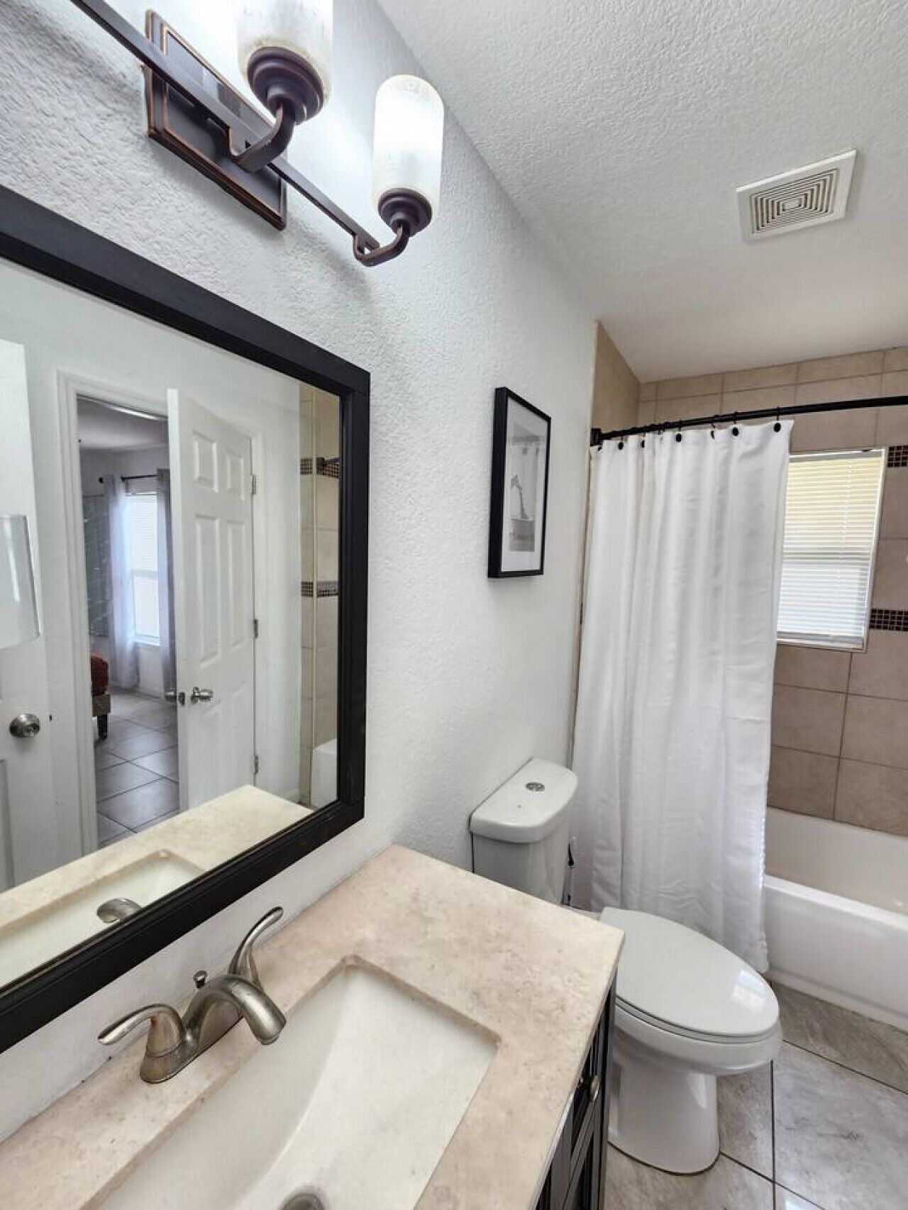 A bathroom with a sink, mirror, toilet, and shower curtain.