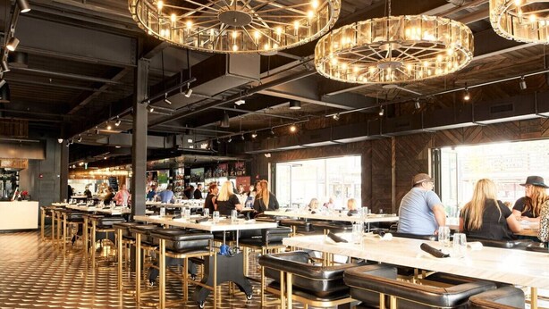 Ein geräumiges Restaurant mit hohen Decken, freiliegenden Balken und moderner Pendelleuchten.