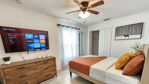 Ein Schlafzimmer mit einem Bett, einer Holzkommode, einem an der Wand montierten Fernseher und einem Deckenventilator.
