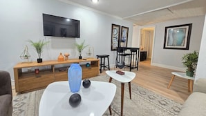 Ein modernes Wohnzimmer mit einem Flachbildfernseher, einem Holztischelement, einem weißen Couchtisch und einem Essbereich mit Tisch und Stühlen.