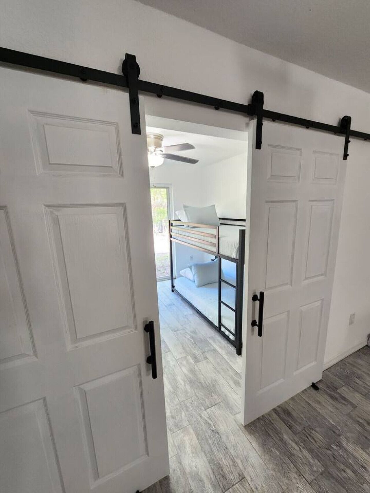 A room with a sliding door leading to a balcony with a bed and a ceiling fan.