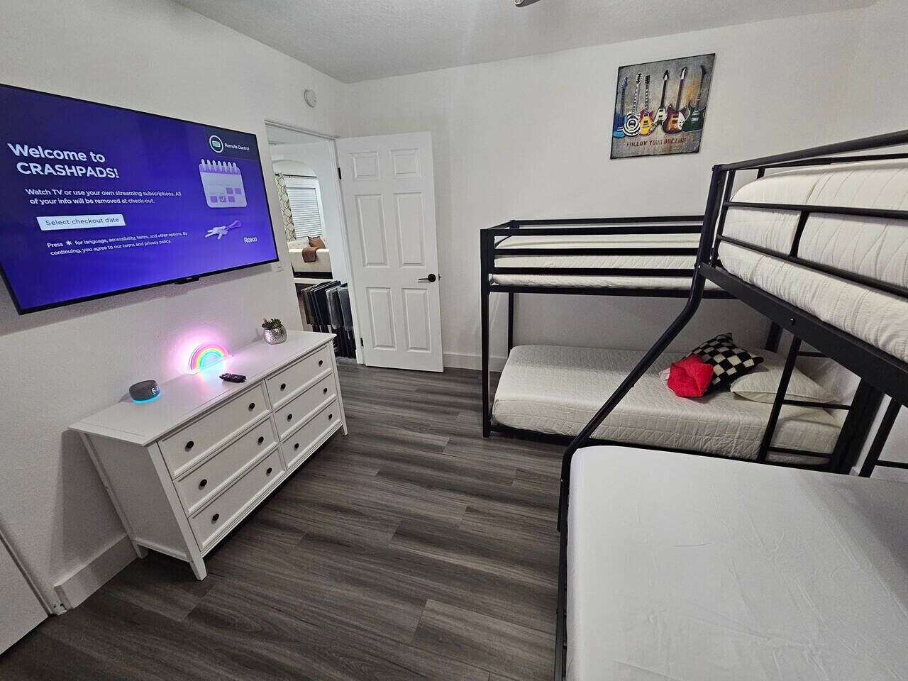 A room with bunk beds, a TV on the wall, a dresser, and a door.