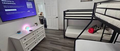 A room with bunk beds, a TV on the wall, a dresser, and a door.