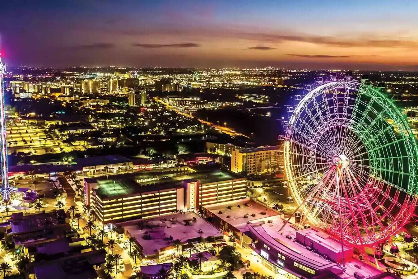 A cityscape at night with a prominent Ferris wheel and a tall building with illuminated windows.