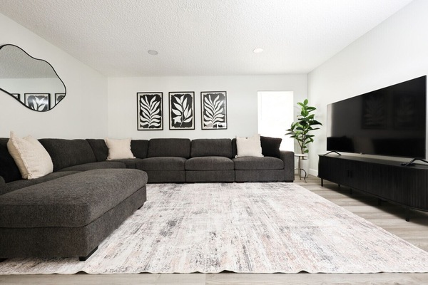 Enjoy a cozy living space with a large L-shaped sectional 🛋️, smart TV 📺, and an open layout that flows into the kitchen and dining area 🍽️.