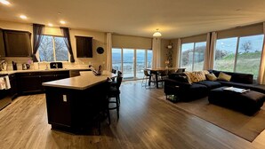 Amplia sala de estar con cocina, mesa de comedor y un ventanal con vistas al exterior.