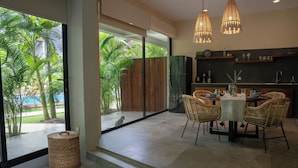 Una cocina moderna con comedor, ventanas amplias y vistas a un jardín tropical.