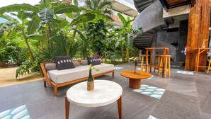 Un área de descanso exterior moderna con un sofá, una mesa de centro y sillas de madera.