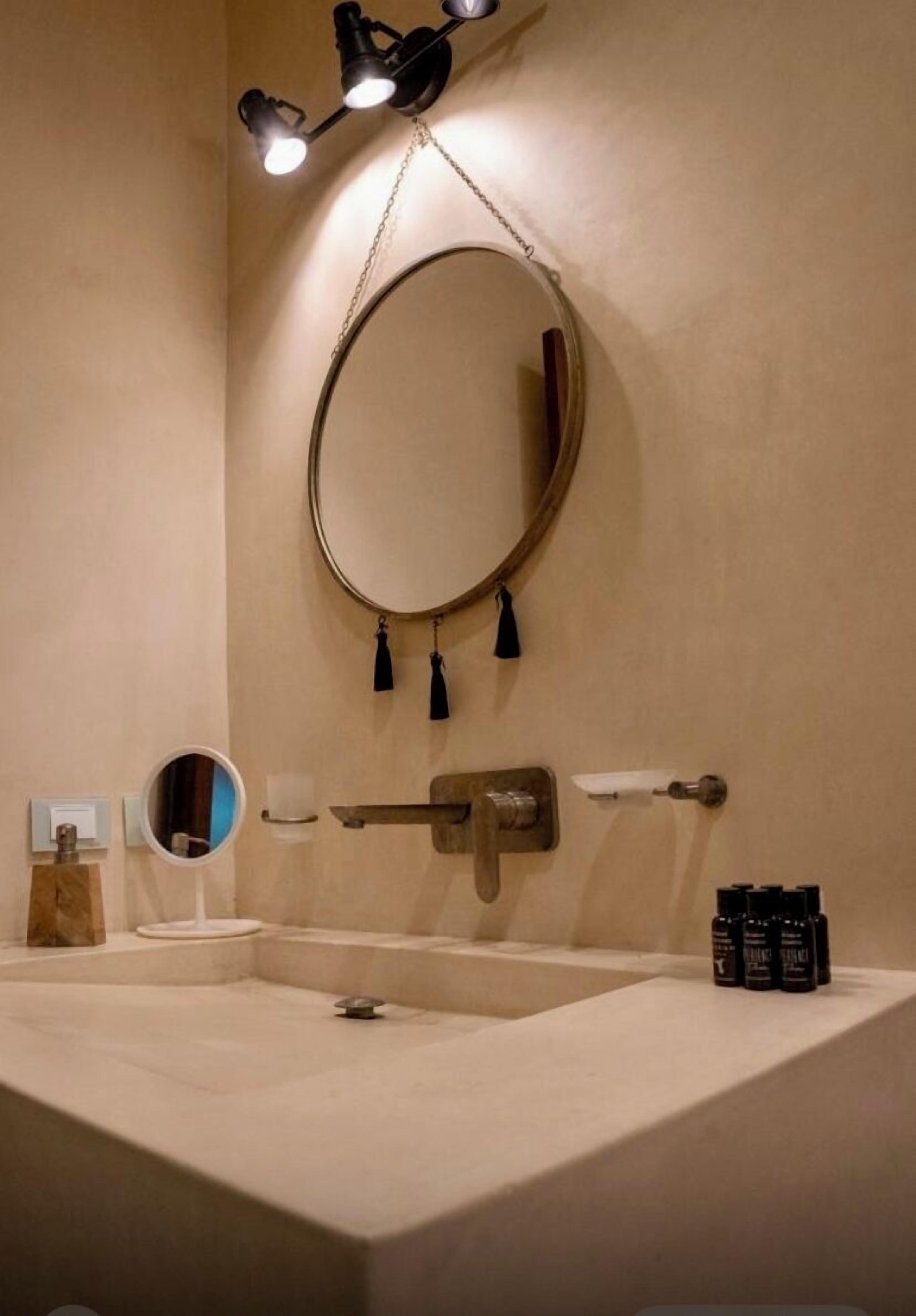 Un bagno con un ampio specchio ovale, un portascopevoli a muro, un erogatore di asciugamani e uno scaffale con articoli da toilette.