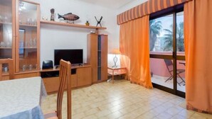 A room with a dining table, a TV, a cabinet with glass doors, and a window with curtains. - Next to Lisbon 100m from Beaches & Surf (Costa da Caparica)