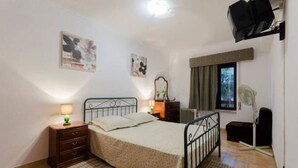 A bedroom with a bed, bedside tables, a nightstand, a radiator, a window with curtains, and wall art. - Next to Lisbon 100m from Beaches & Surf (Costa da Caparica)